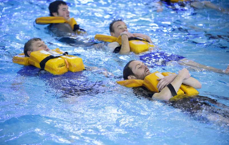 A group of men with flotation devices are floating on their backs in a swimming pool.