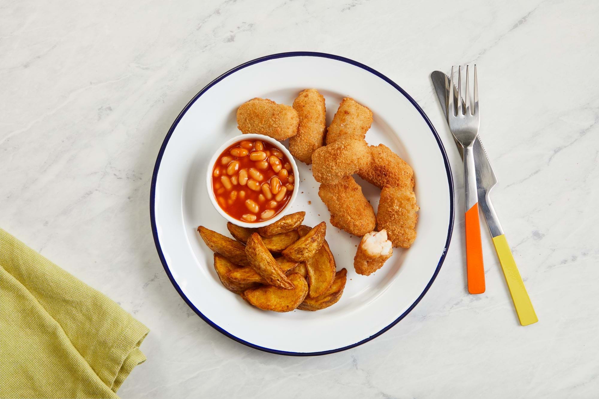 A plate of scampi, potato wedges and beans laid on a table.