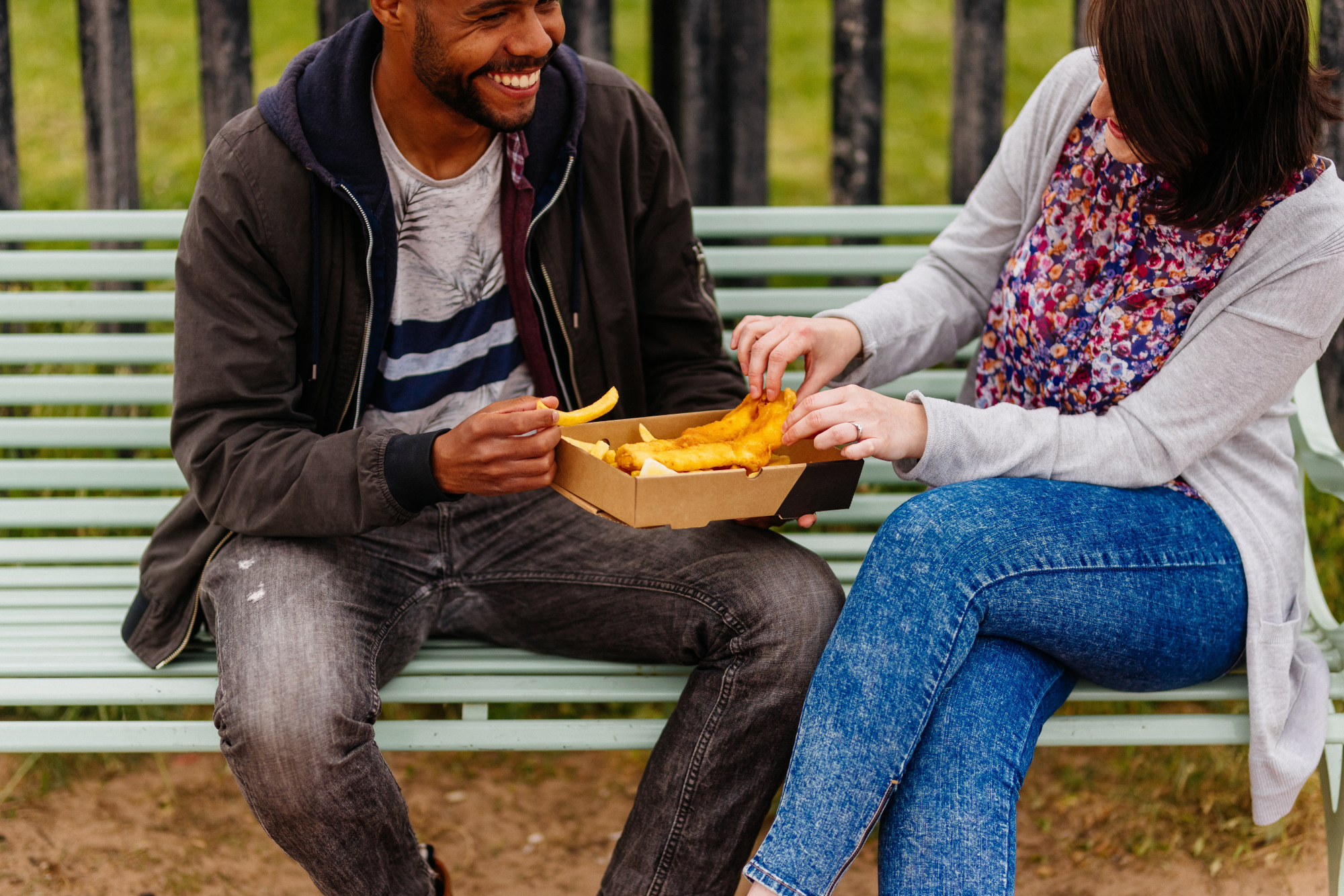 Photo of a couple sitting on a bench eating fish and chips