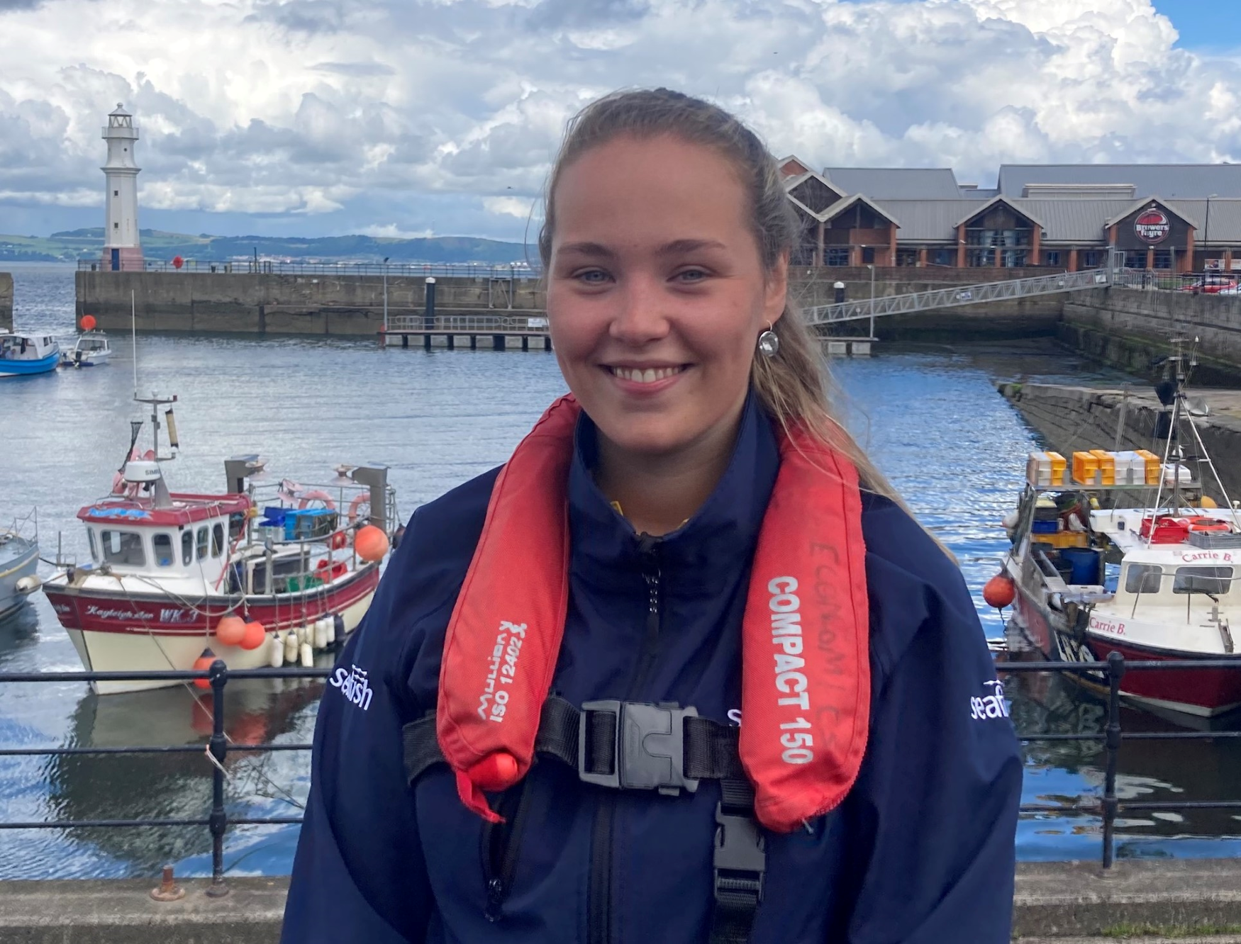 Field Researcher Emma at a harbour in front of fishing boats.