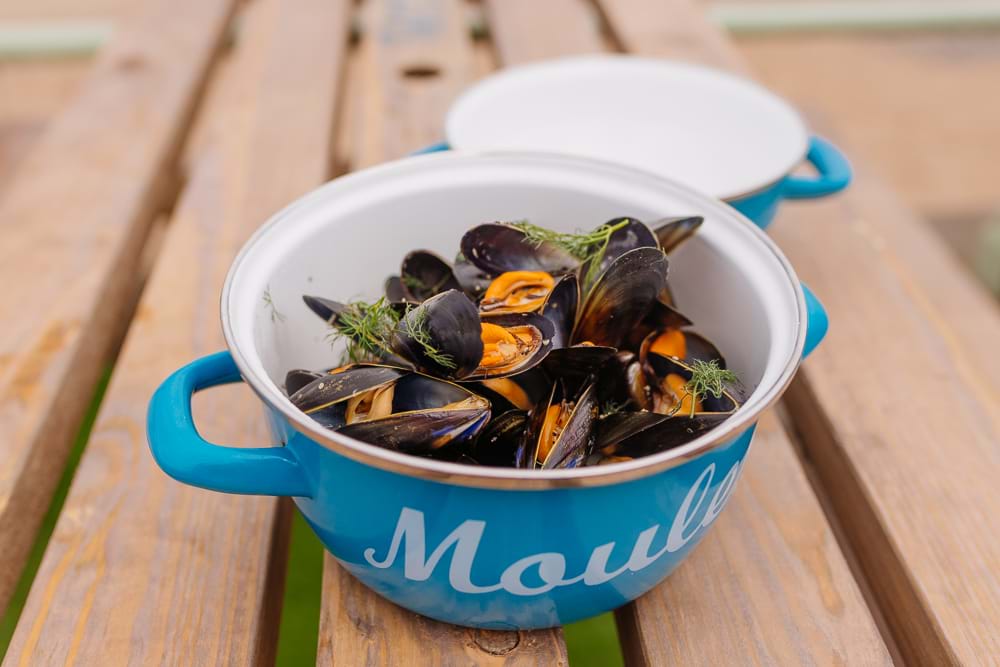 An open pot of cooked mussels on a picnic bench.