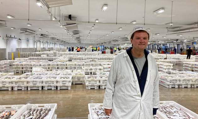 Jack standing in the fish market in front of stacked fish boxes