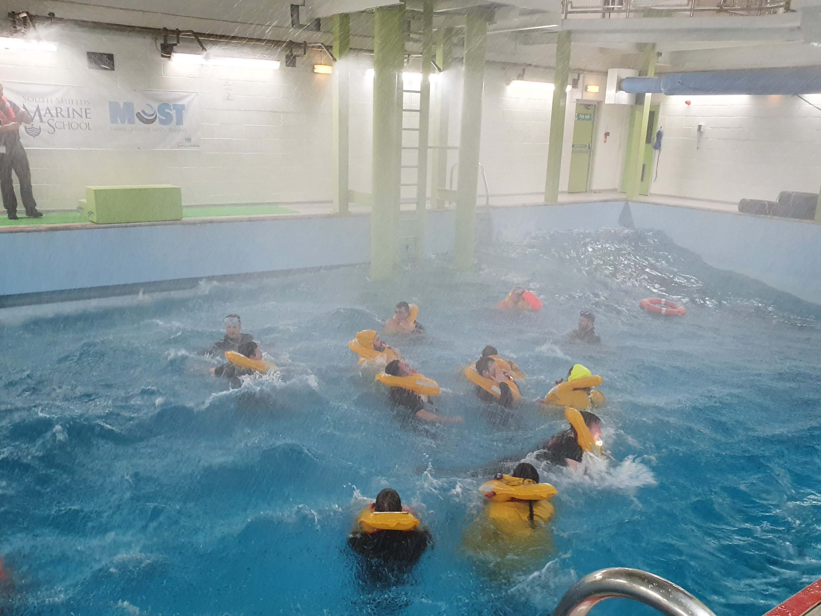 A group of men in a training swimming pool with flotation devices on as part of a training exercise.