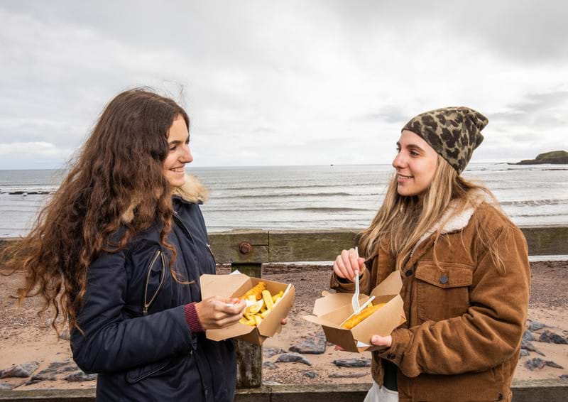 Photo of people eating fish and chips by the shore