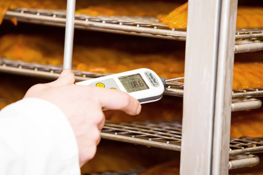 An employee using a digital probe thermometer to check the temperature of smoked fish
