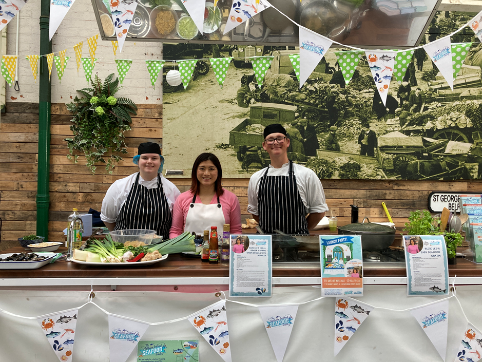 Three people in aprons standing behind kitchen demo counter