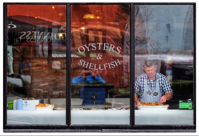 Photo of the outside of Mourne Seafood restaurant. There is a man in the window preparing fish.