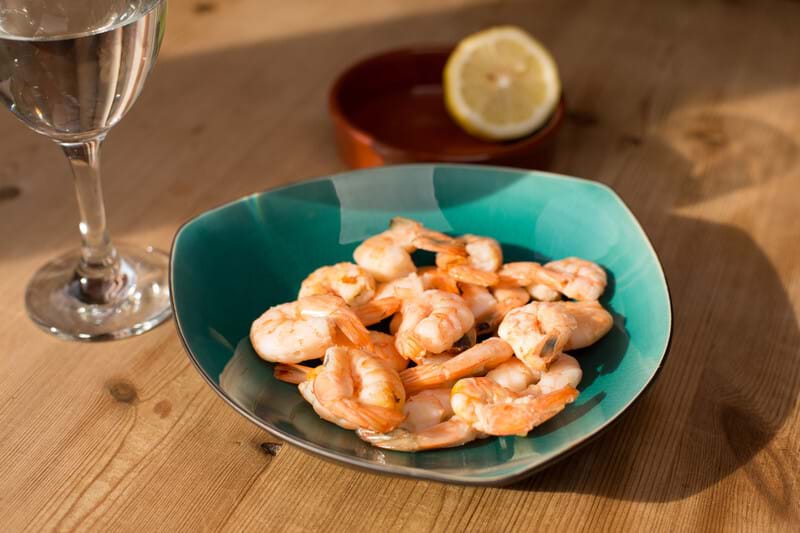 A photo of a cooked prawns in a blue bowl. The bowl is in a dinner setting on a table with a wine glass.