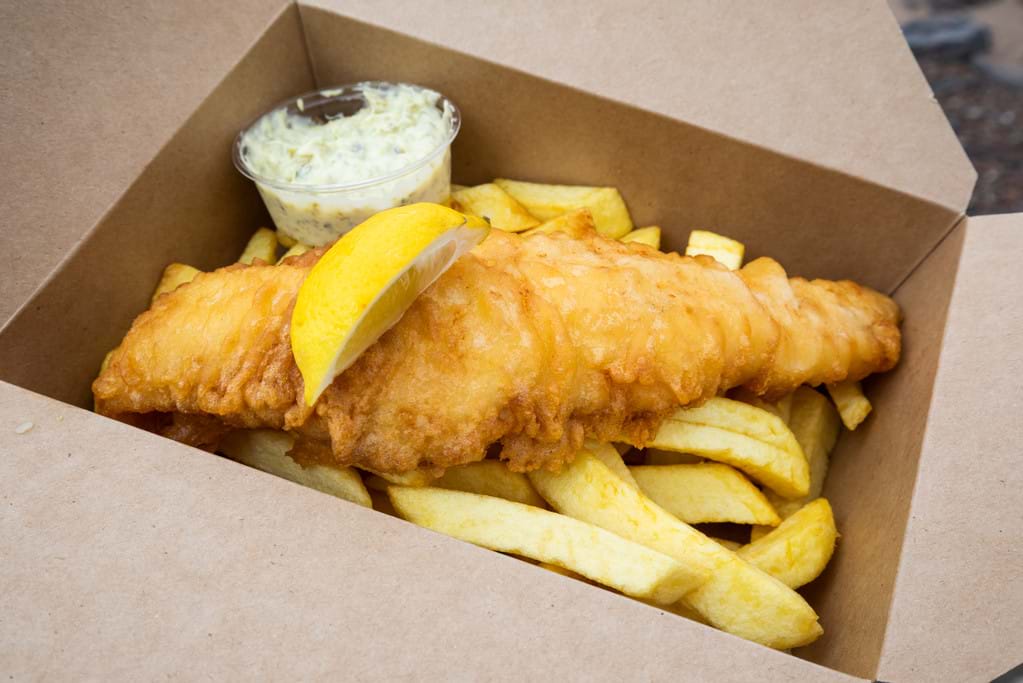 A portion of fish and chips with tarter sauce in a takeaway box